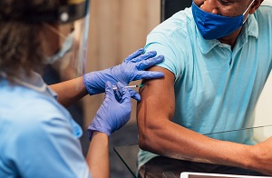 Female doctor administering shot to male patient.